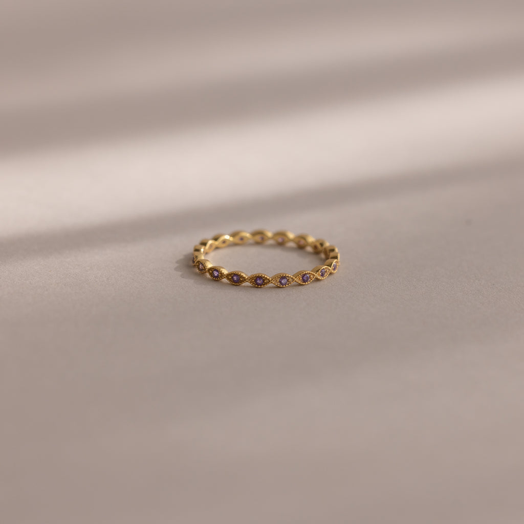 A delicate Dainty Marquise Birthstone Ring in Amethyst (February) rests on a soft beige surface, softly illuminated.