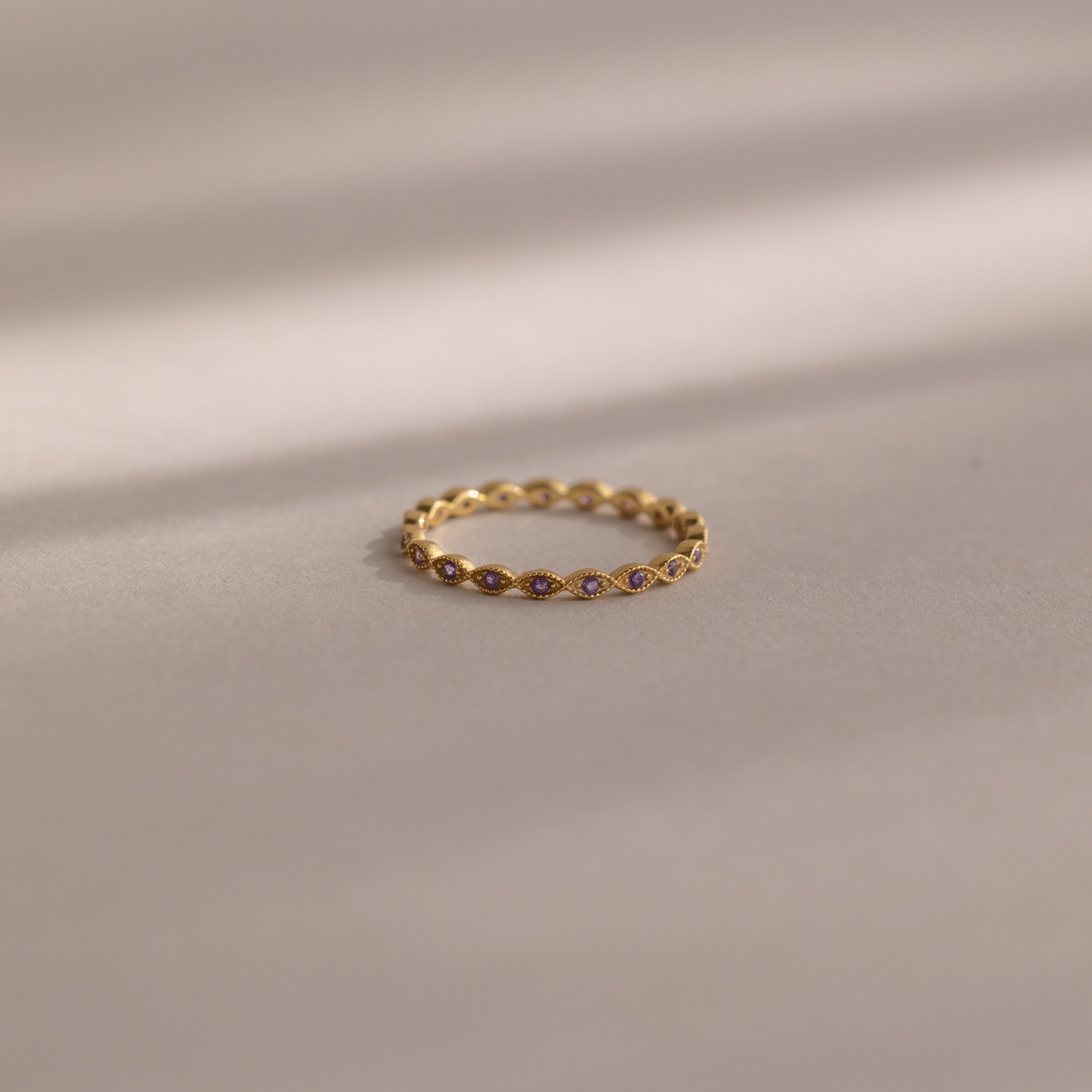 A delicate Dainty Marquise Birthstone Ring in Amethyst (February) rests on a soft beige surface, softly illuminated.