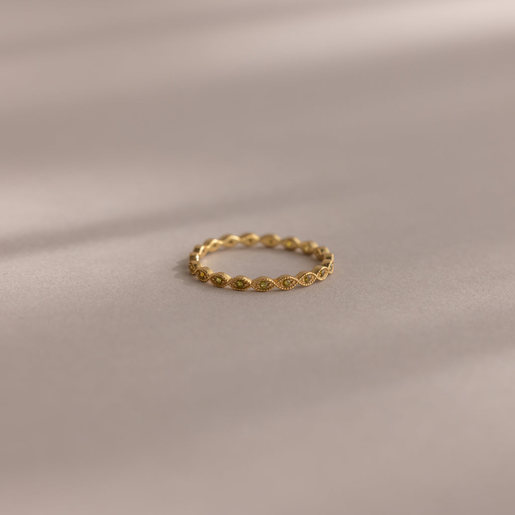 The Dainty Marquise Peridot Ring, featuring a delicate gold Art Deco-inspired twisted design, rests on a soft, neutral surface.