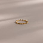 The Dainty Marquise Peridot Ring, featuring a delicate gold Art Deco-inspired twisted design, rests on a soft, neutral surface.