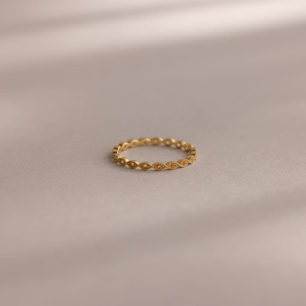 The Dainty Marquise Topaz Ring, featuring a repeating marquise pattern, rests on a smooth, neutral surface with soft shadows.