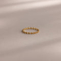 The Dainty Marquise Topaz Ring, featuring a repeating marquise pattern, rests on a smooth, neutral surface with soft shadows.