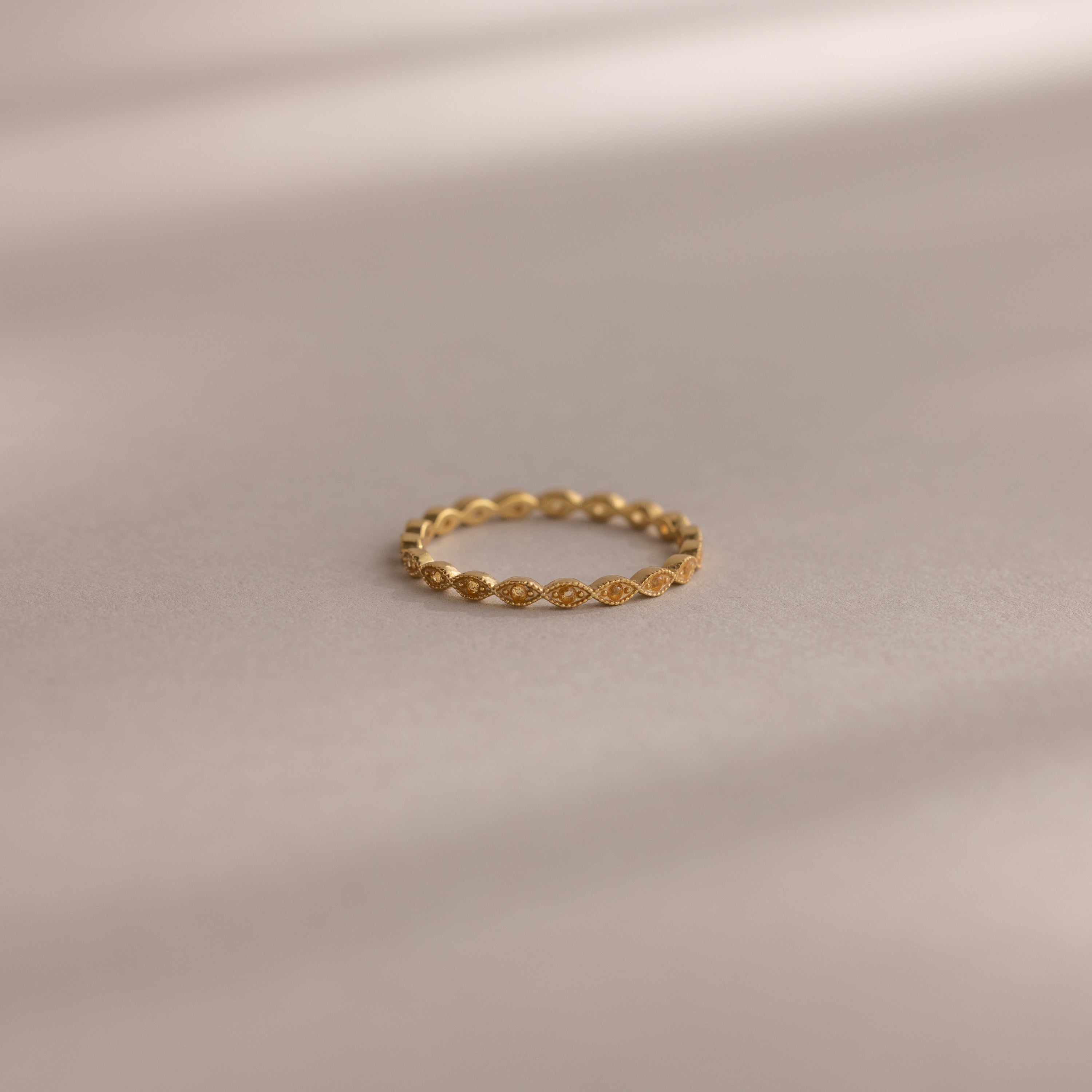 The Dainty Marquise Topaz Ring, featuring a repeating marquise pattern, rests on a smooth, neutral surface with soft shadows.