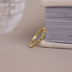 The Dainty Marquise Emerald Ring stands upright against a textured box on a neutral surface, showcasing its delicate design and hint of Art Deco charm.