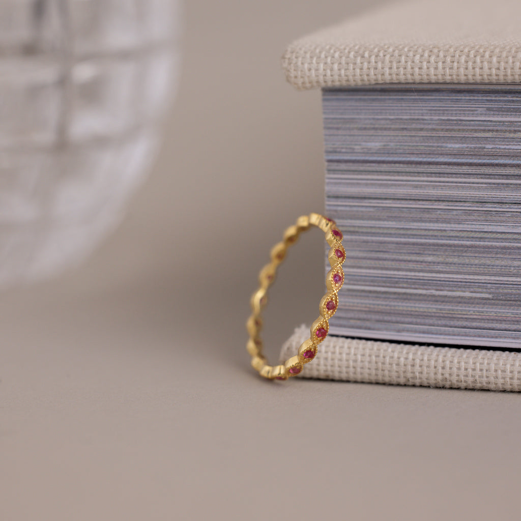The Dainty Marquise Ruby Ring with sparkling red gemstones stands upright against the edge of a closed book.
