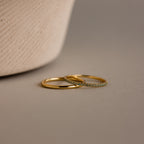 The Birthstone Tennis Ring Set in Aquamarine (March) features two elegant rings—a sleek gold band and a gemstone eternity ring—gracefully displayed on a neutral surface.