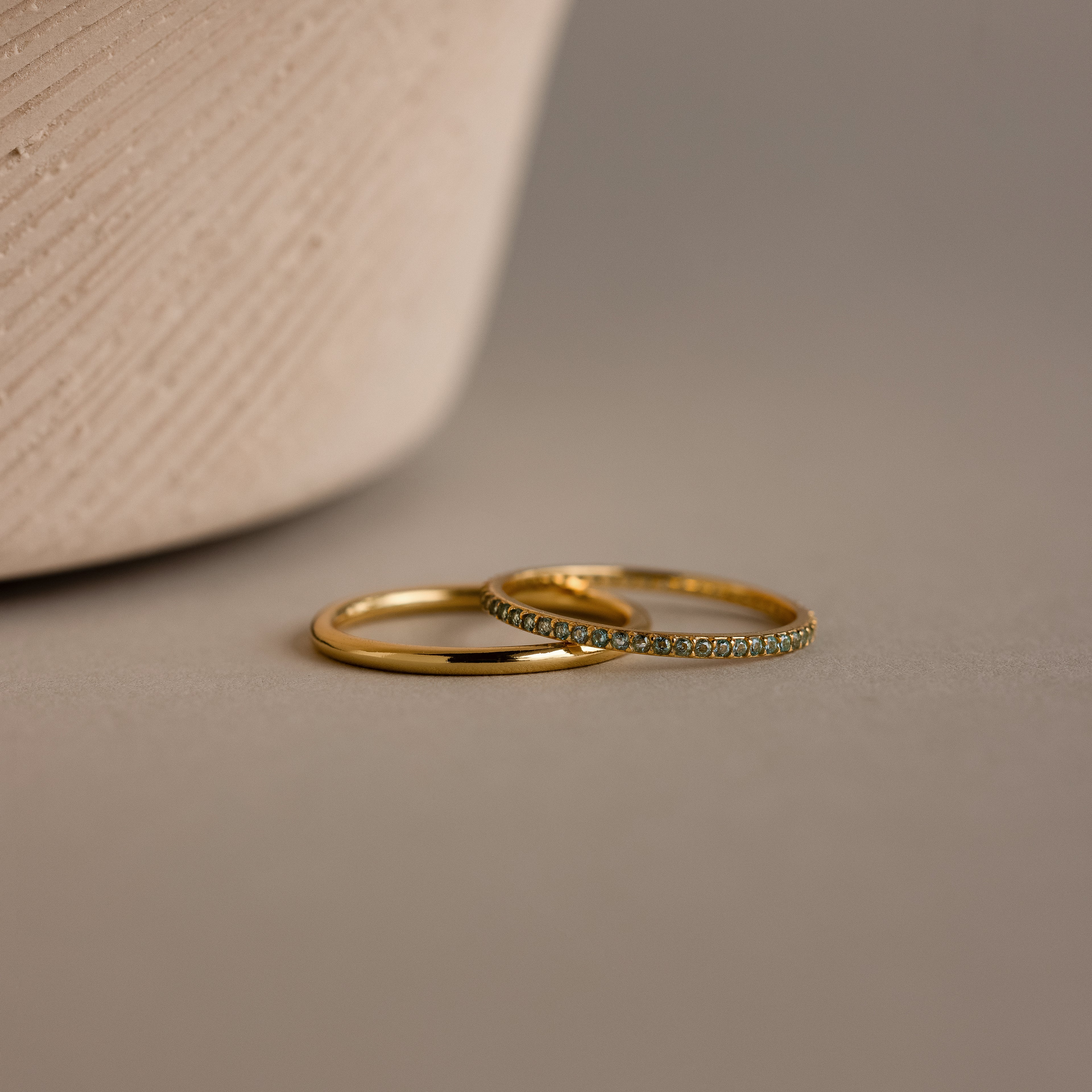 The Birthstone Tennis Ring Set in Aquamarine (March) features two elegant rings—a sleek gold band and a gemstone eternity ring—gracefully displayed on a neutral surface.