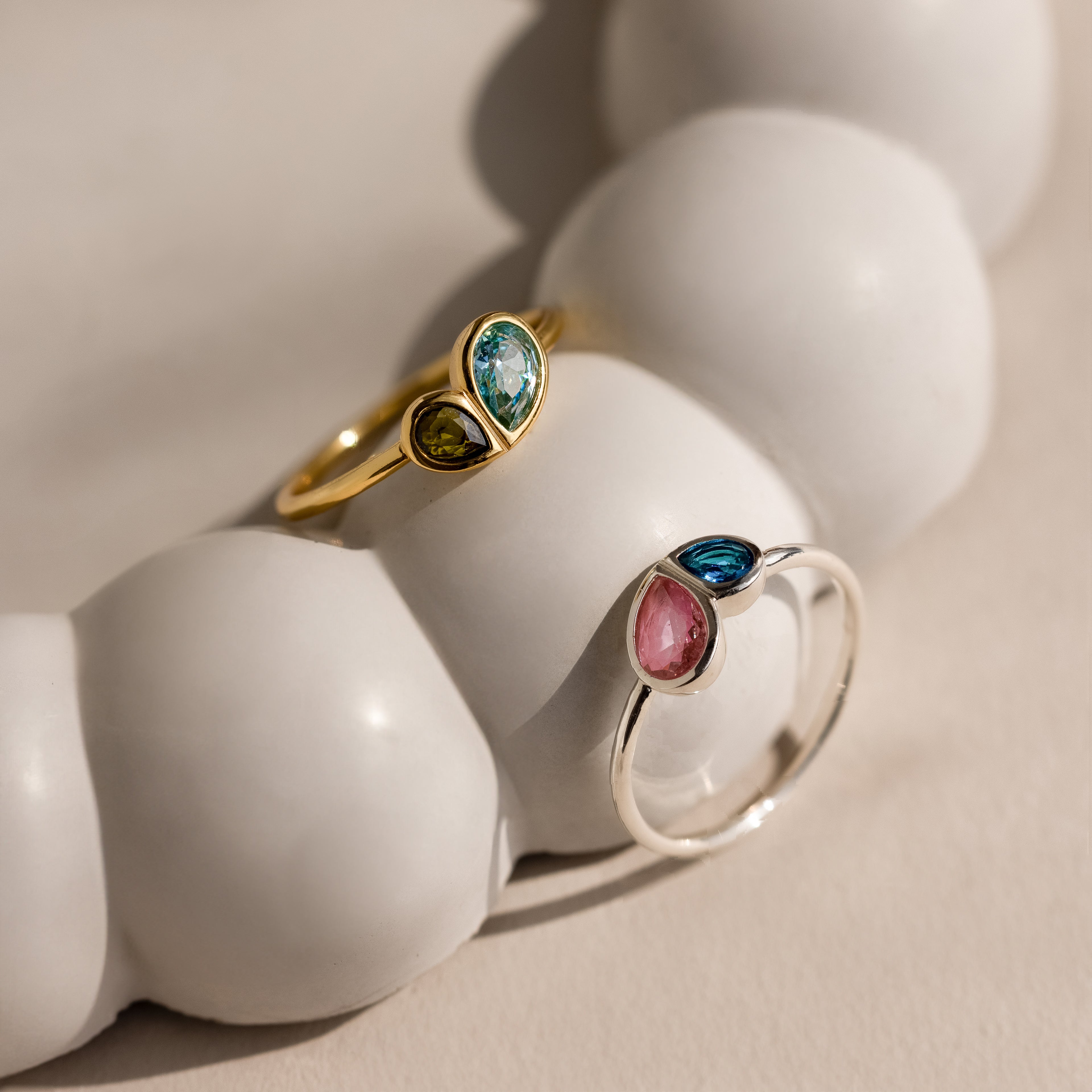 The Toi et Moi Heart Birthstone Ring in Rose Gold is displayed on a smooth, white, rounded surface.