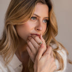 A woman with wavy blonde hair wears the Toi et Moi Heart Birthstone Ring in 18K Gold, featuring a green gemstone, as she gazes thoughtfully to the side.
