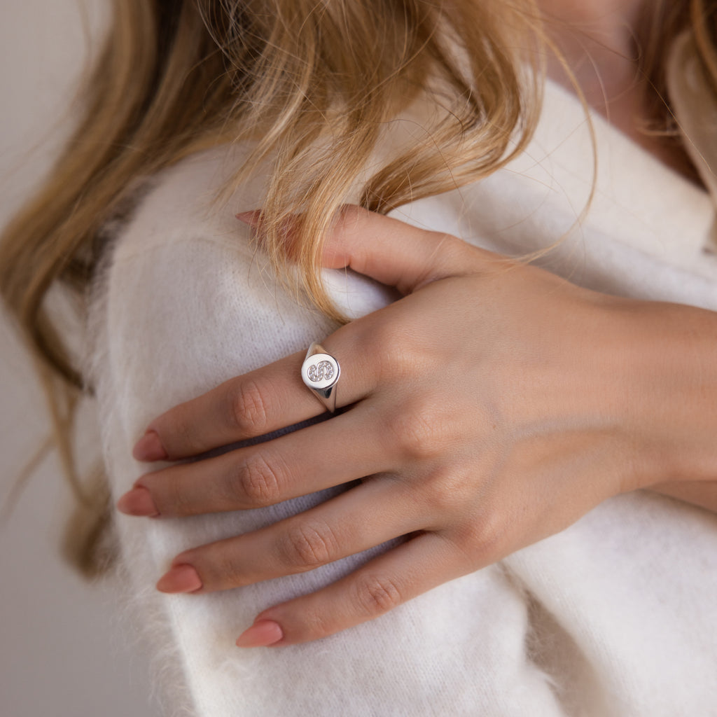 A woman with long blonde hair wears the Pave Initial Signet Ring in Sterling Silver on her finger and rests her hand on her shoulder.