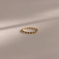 The Dainty Marquise Onyx Ring, a delicate gold Art Deco design with small, evenly spaced round accents, rests on a soft beige surface with gentle shadows.