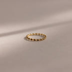 The Dainty Marquise Onyx Ring, a delicate gold Art Deco design with small, evenly spaced round accents, rests on a soft beige surface with gentle shadows.