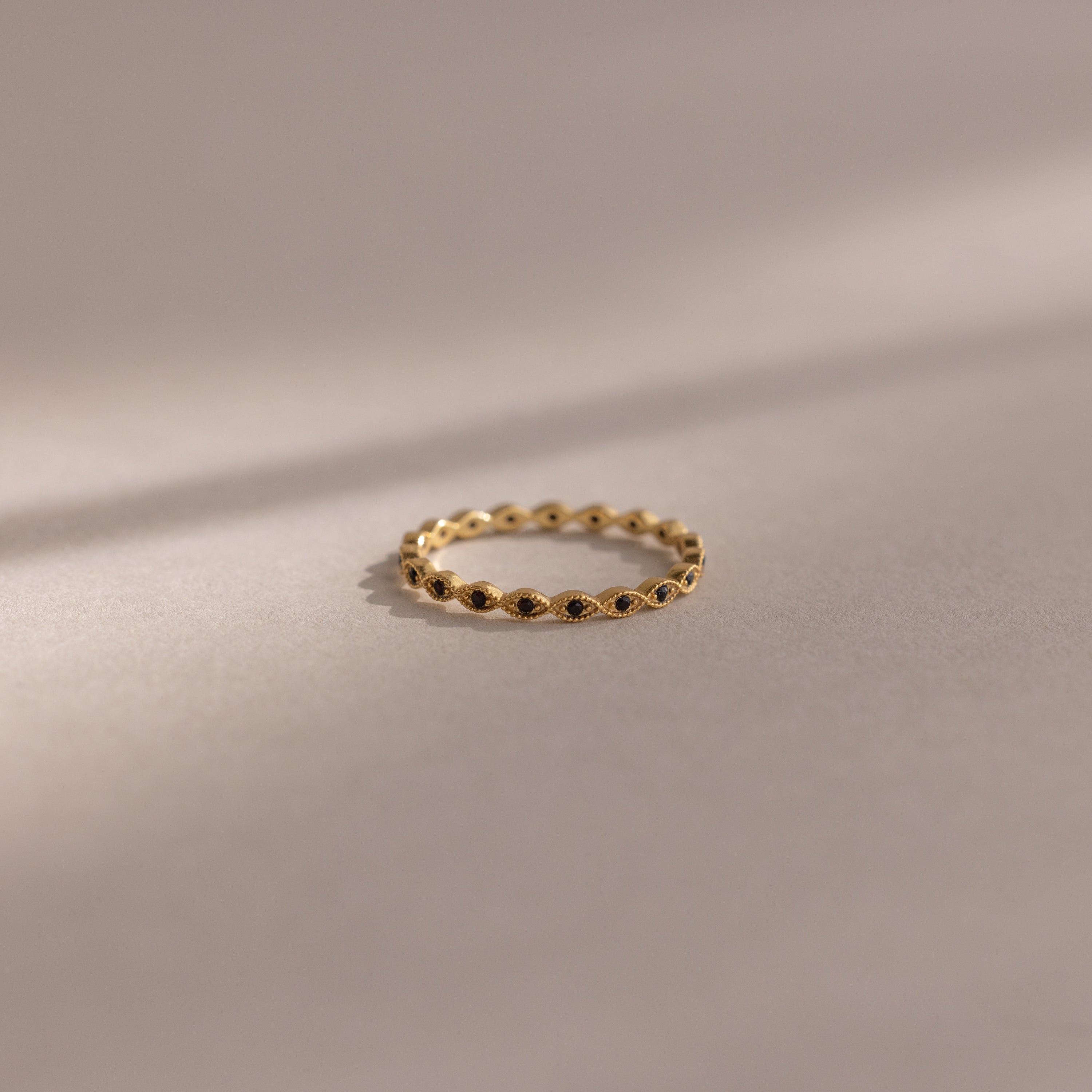 The Dainty Marquise Onyx Ring, a delicate gold Art Deco design with small, evenly spaced round accents, rests on a soft beige surface with gentle shadows.