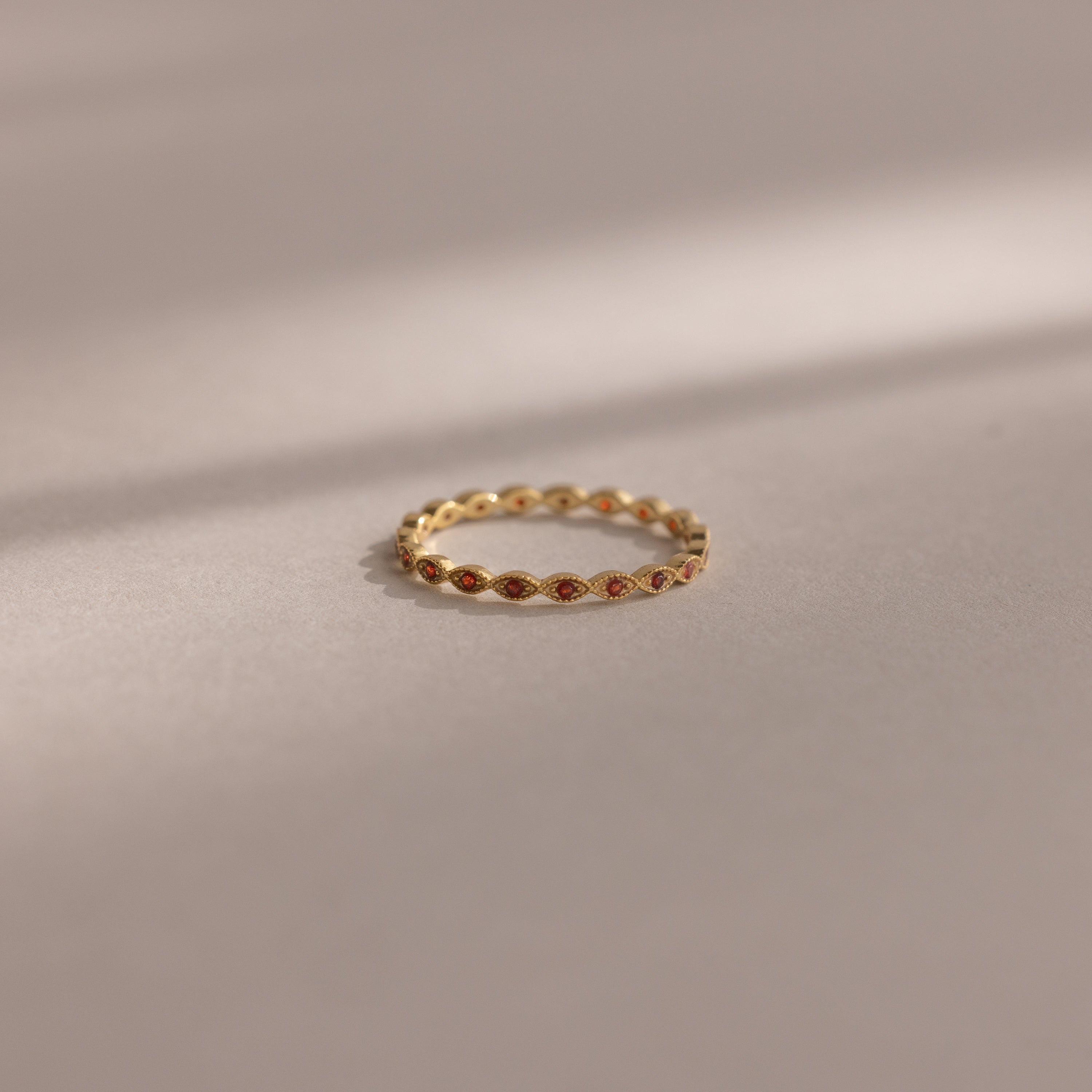 A Dainty Marquise Birthstone Ring in Garnet (January) rests on a soft, neutral surface under gentle lighting.
