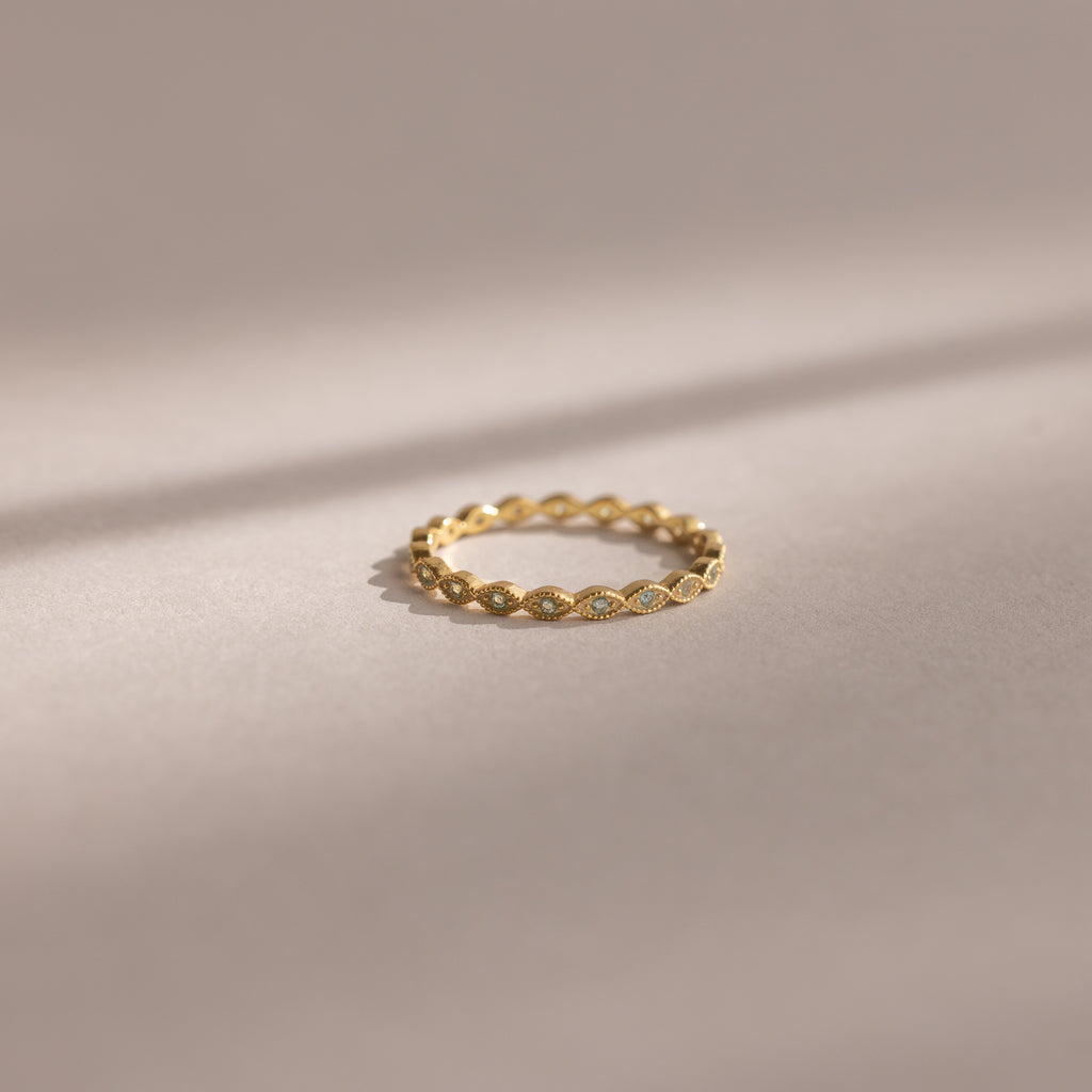 The Dainty Marquise Aquamarine Ring, featuring a delicate gold setting and intricate twisted design, rests on a soft neutral background.