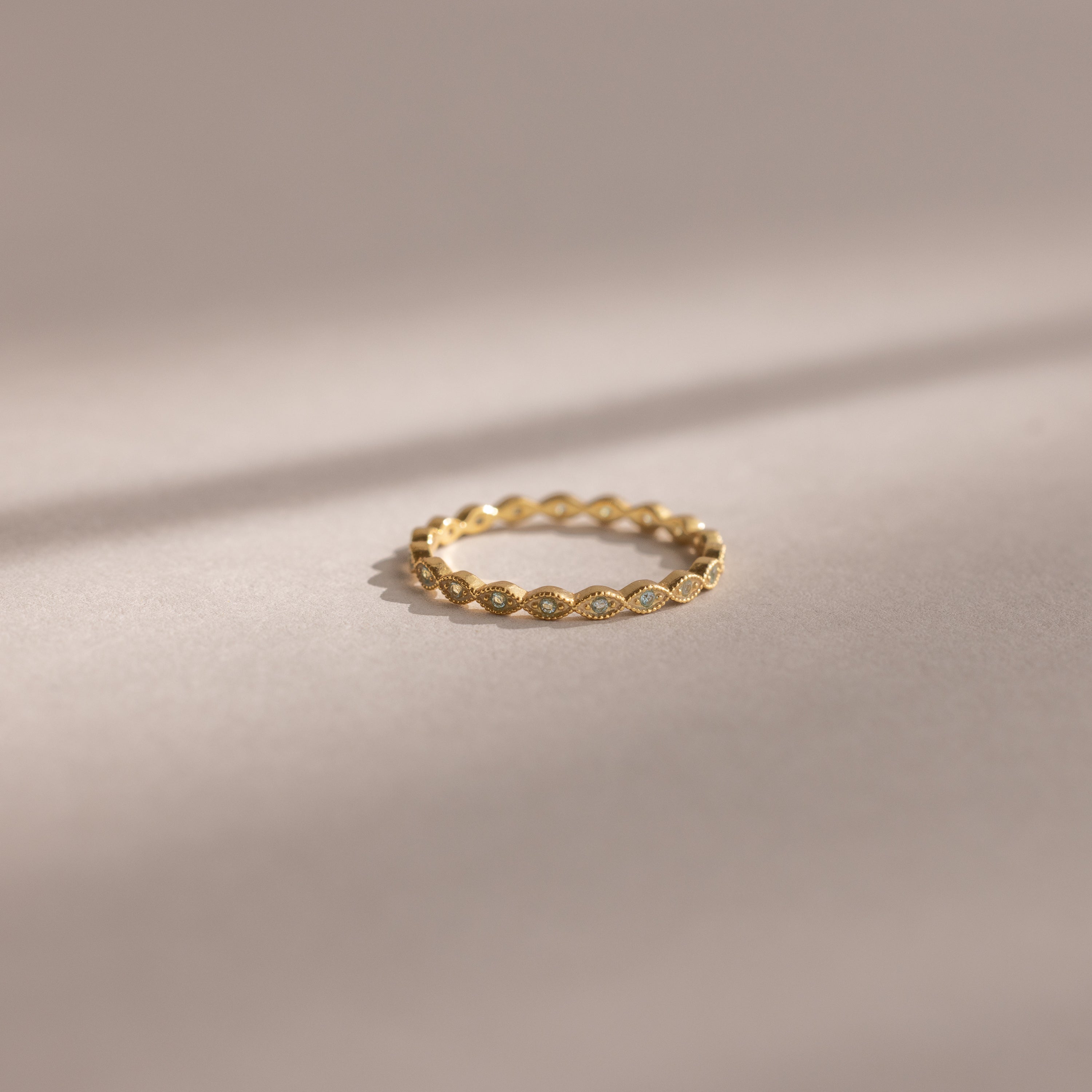 The Dainty Marquise Aquamarine Ring, featuring a delicate gold setting and intricate twisted design, rests on a soft neutral background.