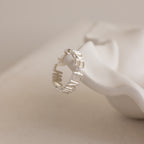 A Multiple Name Eternity Ring in sterling silver, displayed on a white sculptural surface, personalized with the word PEACE.