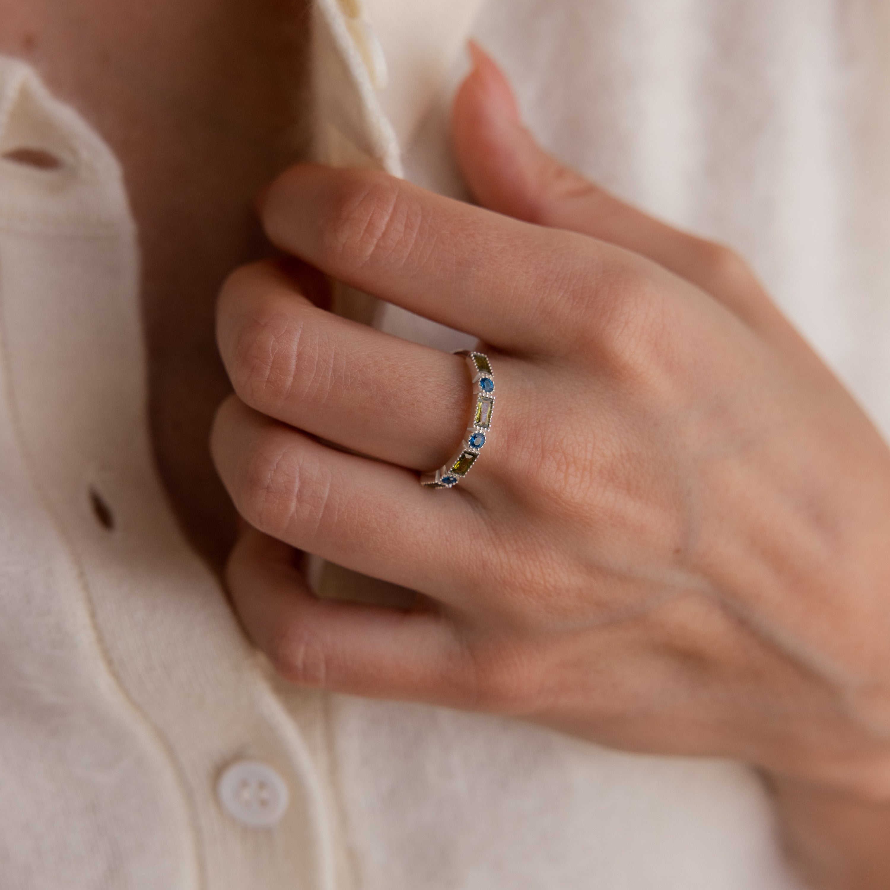 A hand showcases the Mixed Art Deco Birthstone Ring in Sterling Silver, adorned with colorful gemstones, resting on a cream-colored button-up shirt.