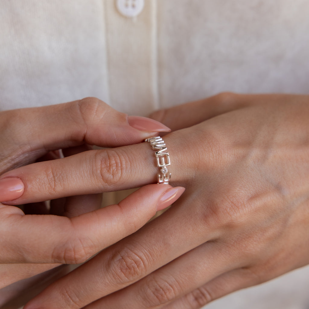 A person wearing the Multiple Name Eternity Ring in Sterling Silver, engraved with custom names, adjusts it on their finger with the other hand.