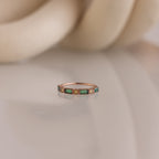 The Mixed Art Deco Birthstone Ring in Rose Gold features square green stones and small diamonds, elegantly displayed on a reflective surface.