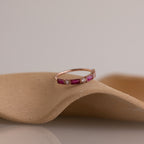 The Mixed Art Deco Birthstone Ring in Rose Gold, featuring pink stones and small diamonds, is displayed on a curved beige surface.