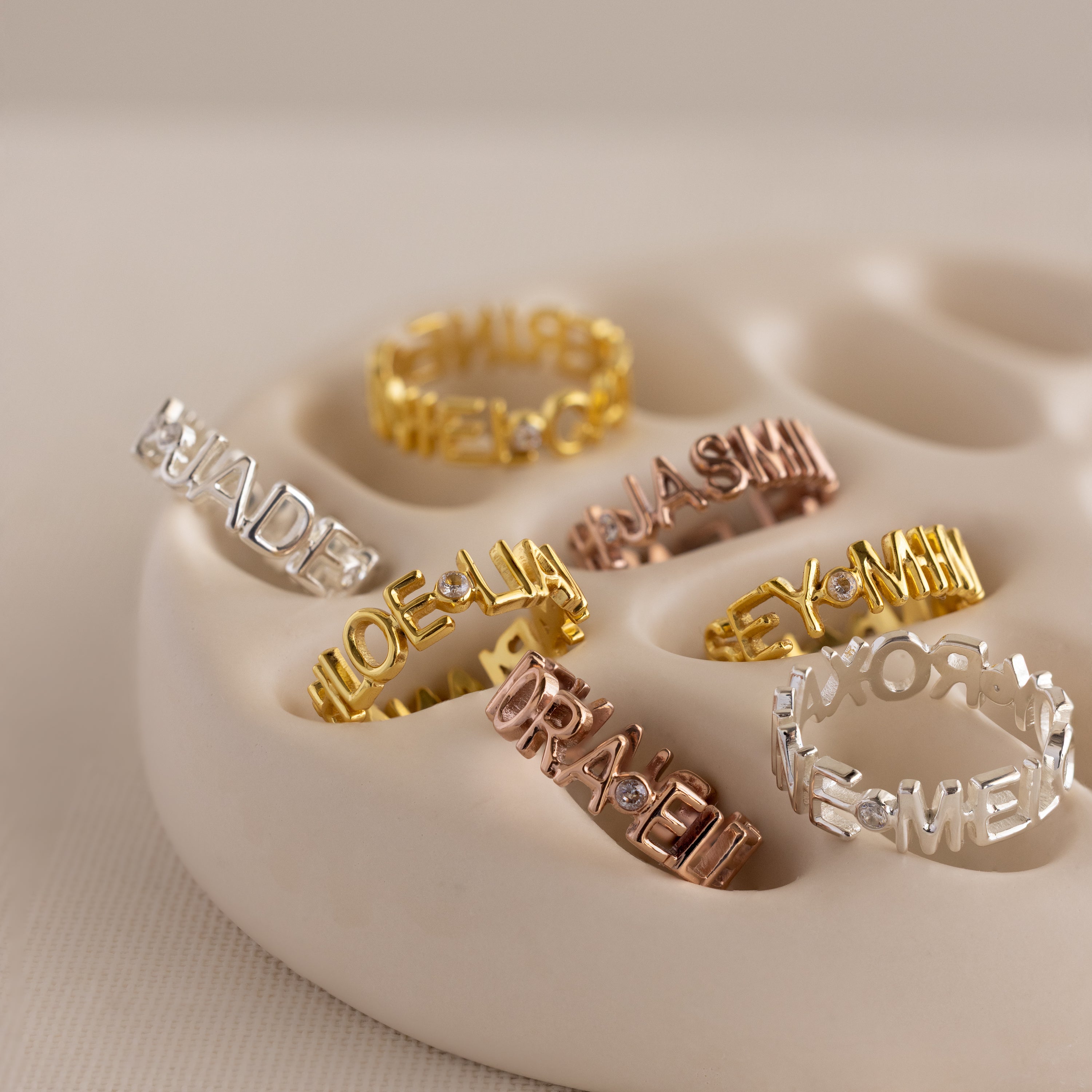 A Multiple Name Eternity Ring in Rose Gold, engraved with names, sits on a cream ceramic dish—each personalized ring is a unique keepsake.
