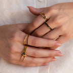 Close-up of hands with manicured nails wearing multiple gold rings, including the Staggered Marquise Birthstone Ring.