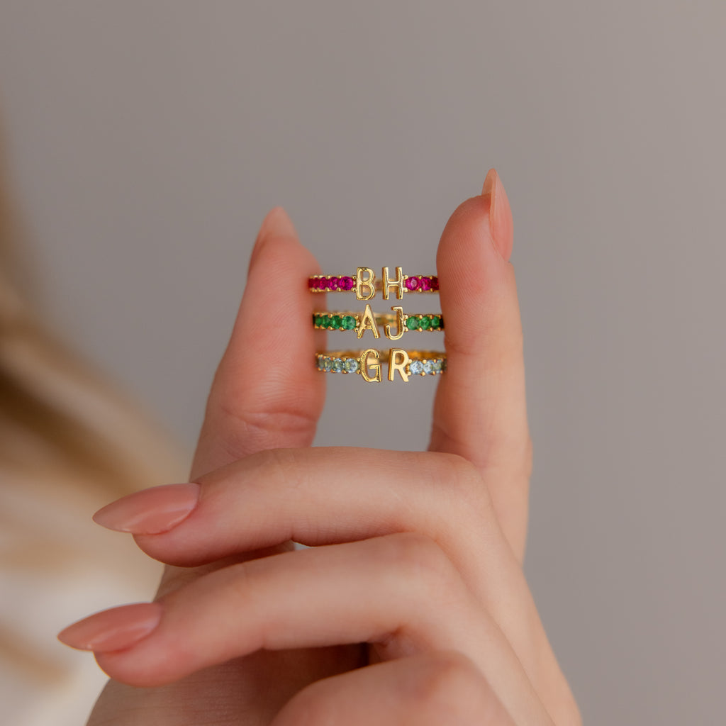 A hand displays the Duo Initial Topaz Tennis Ring, featuring vibrant birthstones and two gold letter charms—ideal for a personalized eternity band or custom initial ring style.
