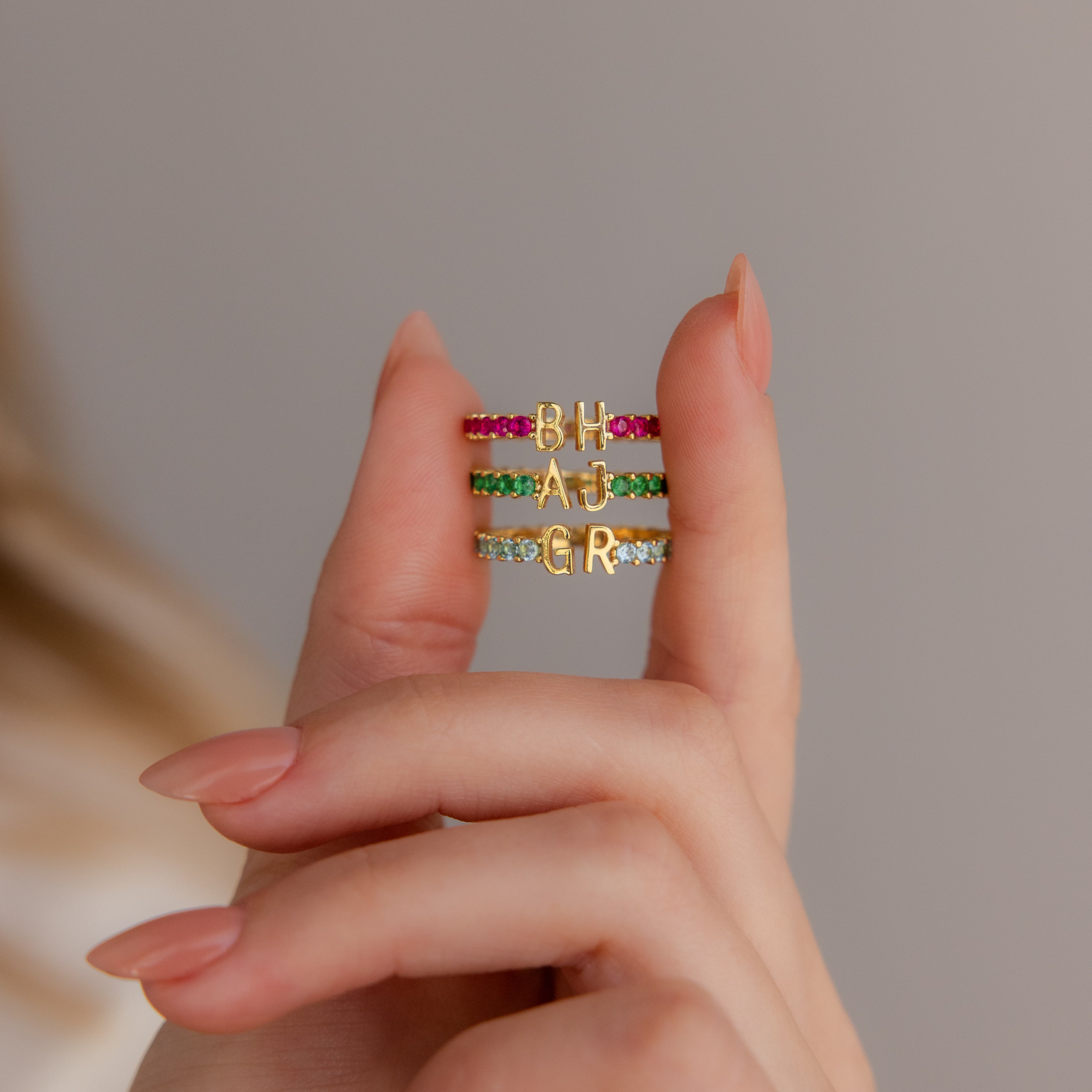 A hand displays the Duo Initial Topaz Tennis Ring, featuring vibrant birthstones and two gold letter charms—ideal for a personalized eternity band or custom initial ring style.