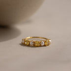 The Topaz & Pearl Lace Ring features a gold band adorned with yellow topaz gemstones and delicate white pearl-like beads, beautifully displayed on a neutral surface under soft lighting.