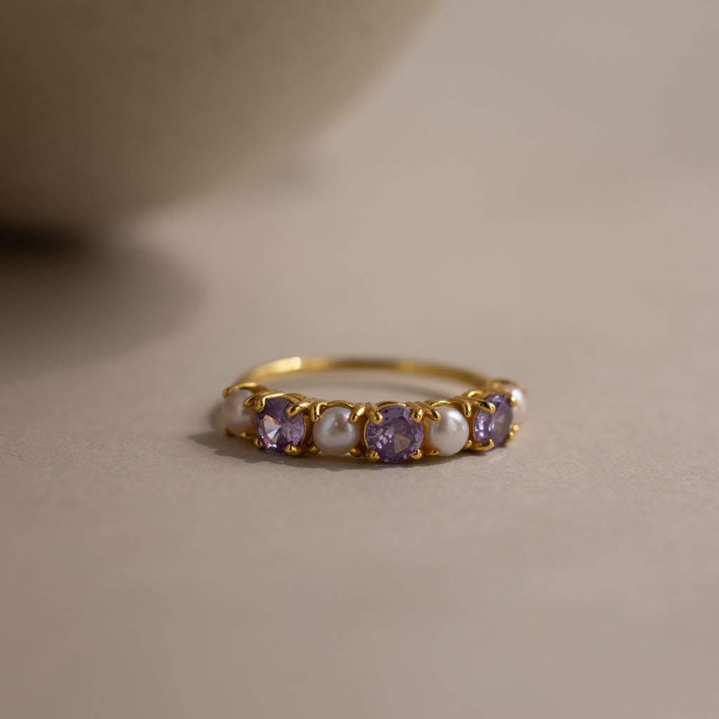 The Birthstone & Pearl Lace Ring in Amethyst (February) features alternating purple gemstones and pearls, shown on a neutral surface.