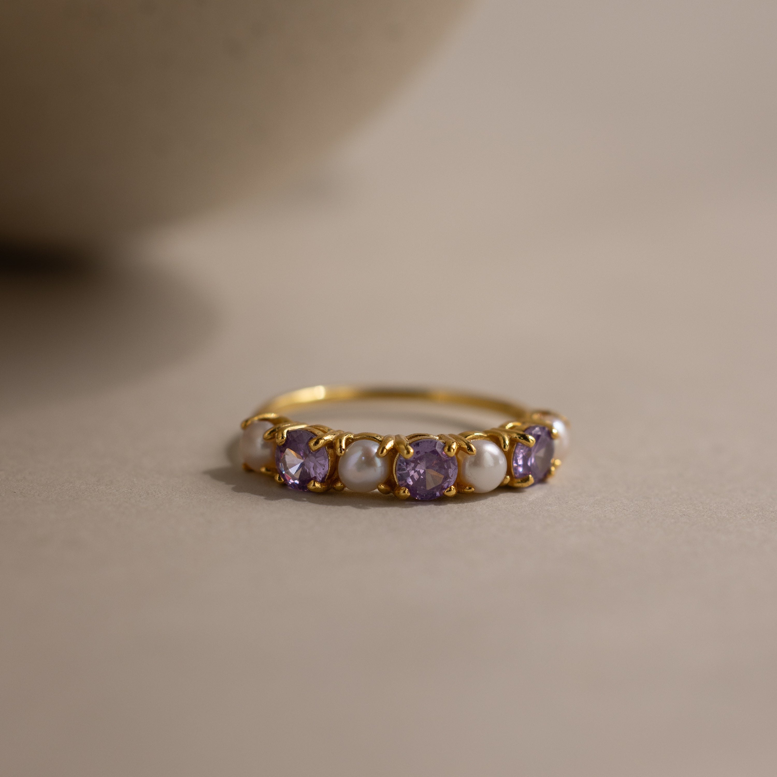 The Birthstone & Pearl Lace Ring in Amethyst (February) features alternating purple gemstones and pearls, shown on a neutral surface.