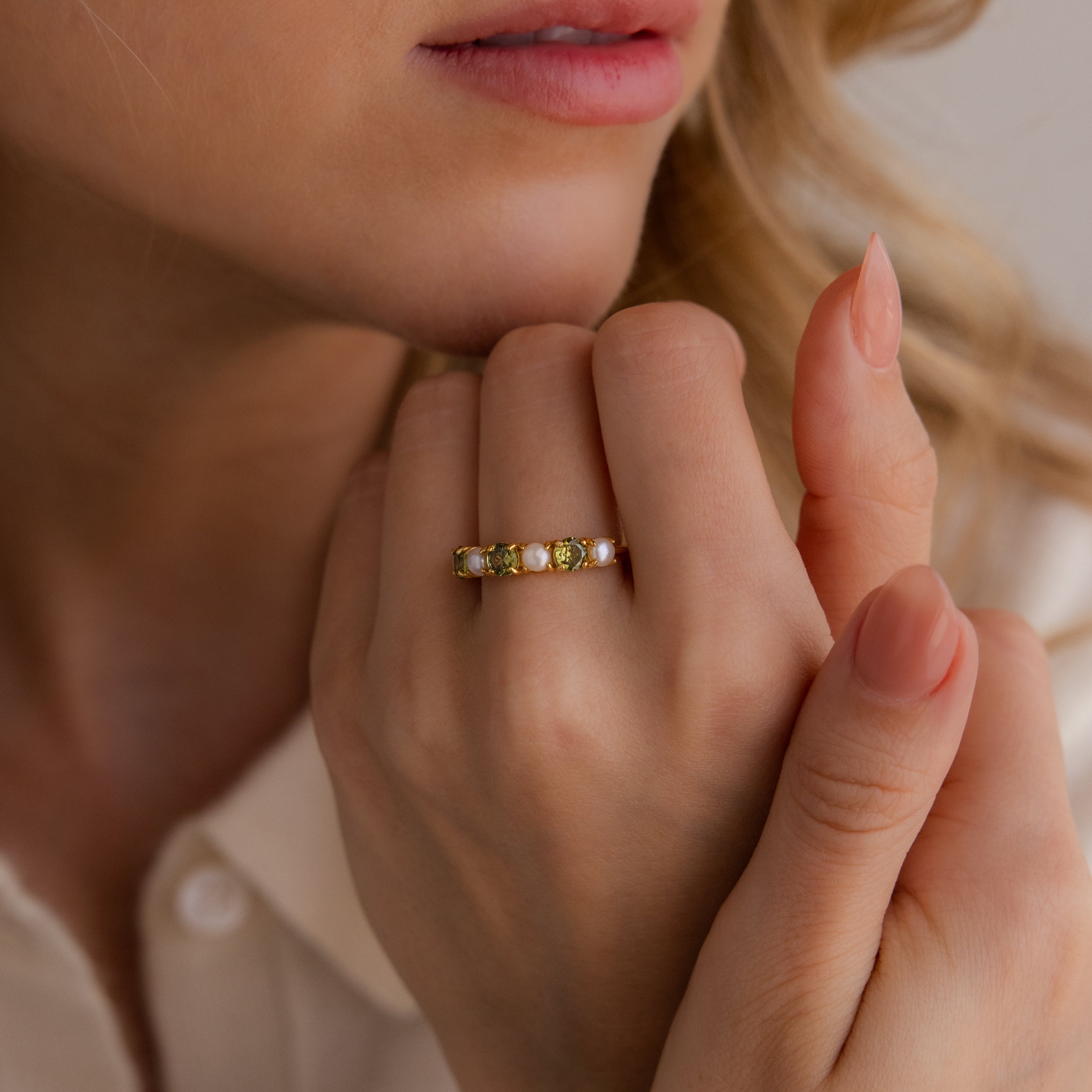 A woman with manicured nails wears the Sapphire & Pearl Lace Ring, a gold band adorned with yellow gemstones, on her finger.