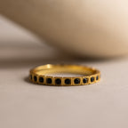 The Art Deco Onyx Eternity Ring features a vintage-inspired gold band adorned with small black onyx stones set in a continuous row, displayed against a neutral background.