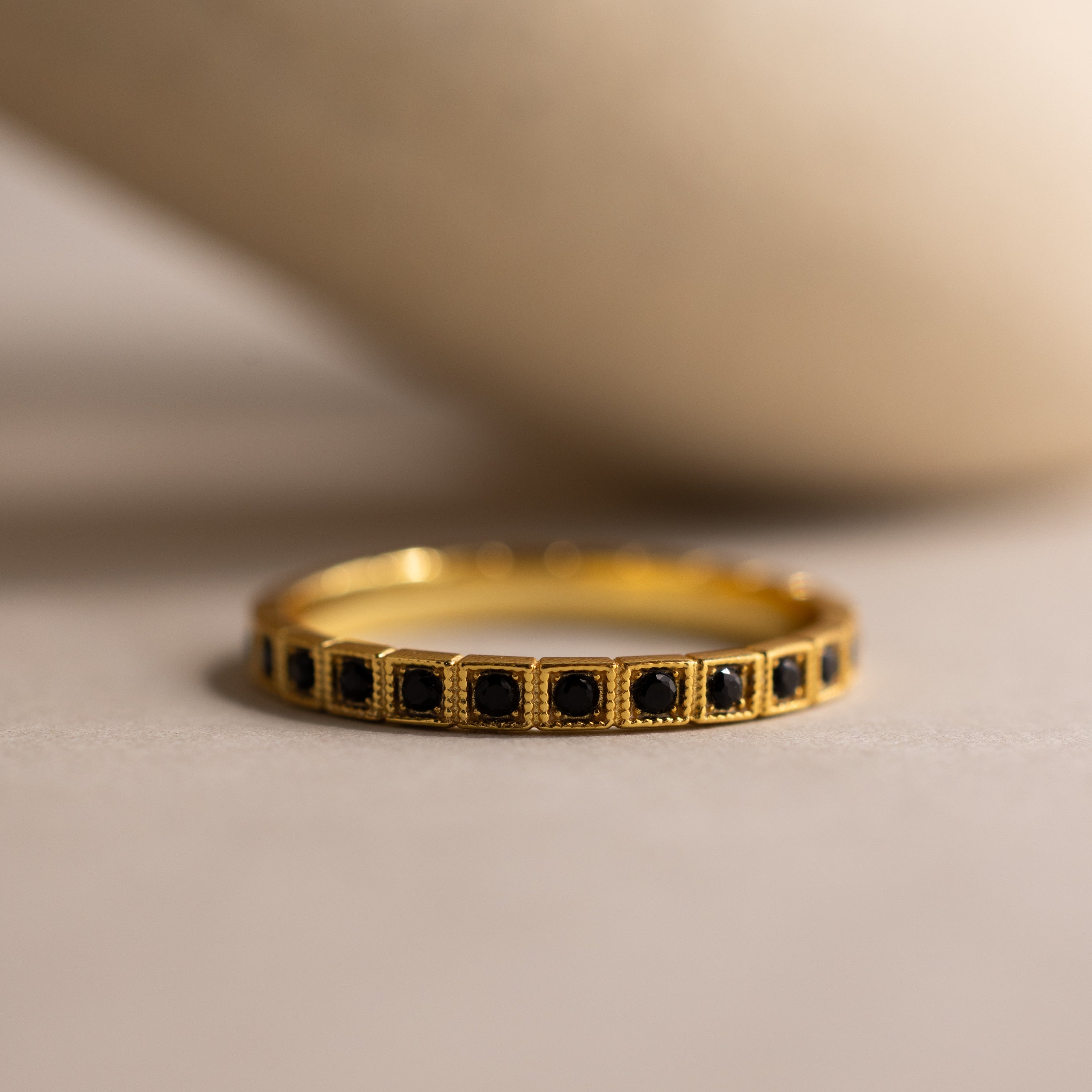 The Art Deco Onyx Eternity Ring features a vintage-inspired gold band adorned with small black onyx stones set in a continuous row, displayed against a neutral background.
