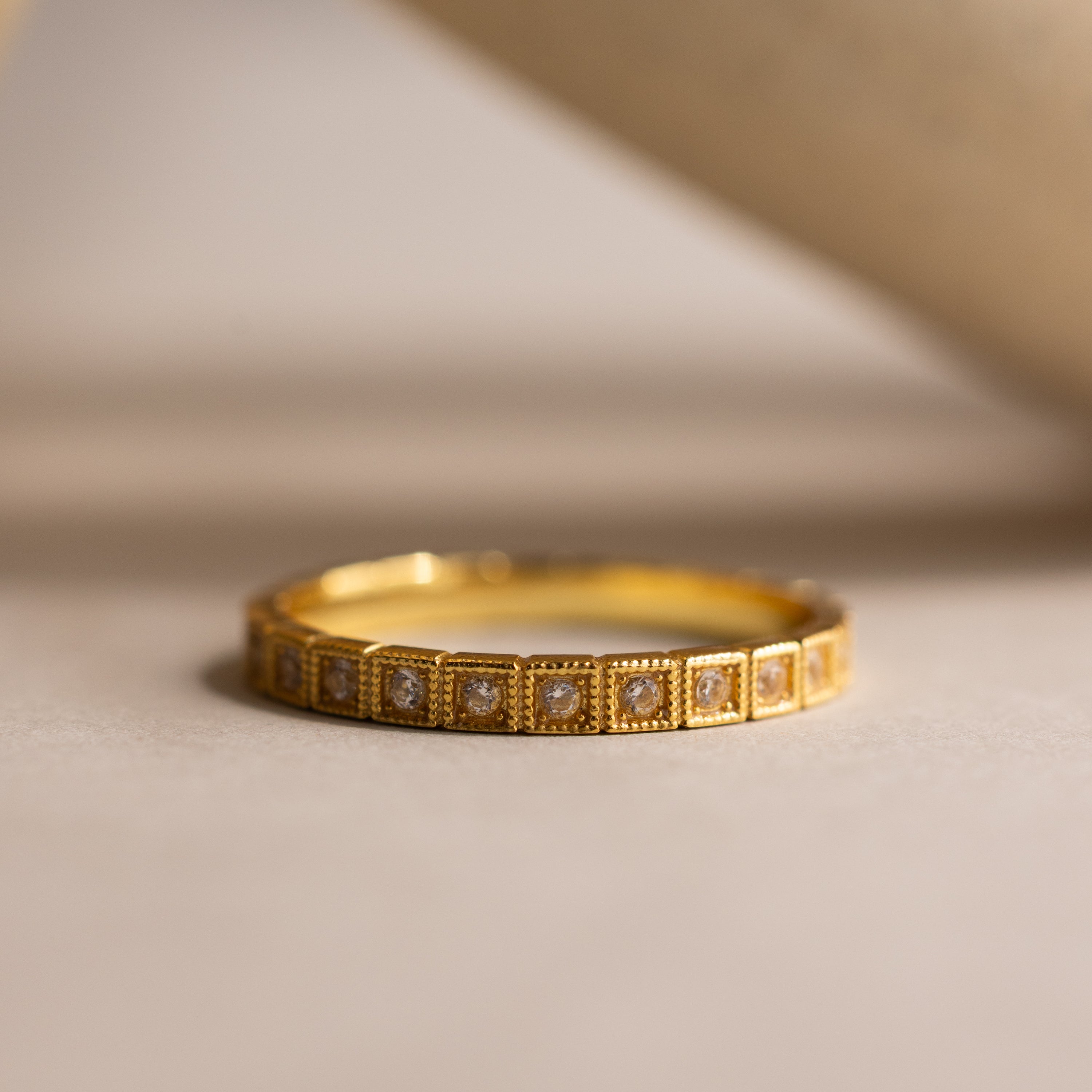 The Art Deco Diamond Eternity Ring features a gold band with small square-shaped diamond settings, showcased on a neutral surface.