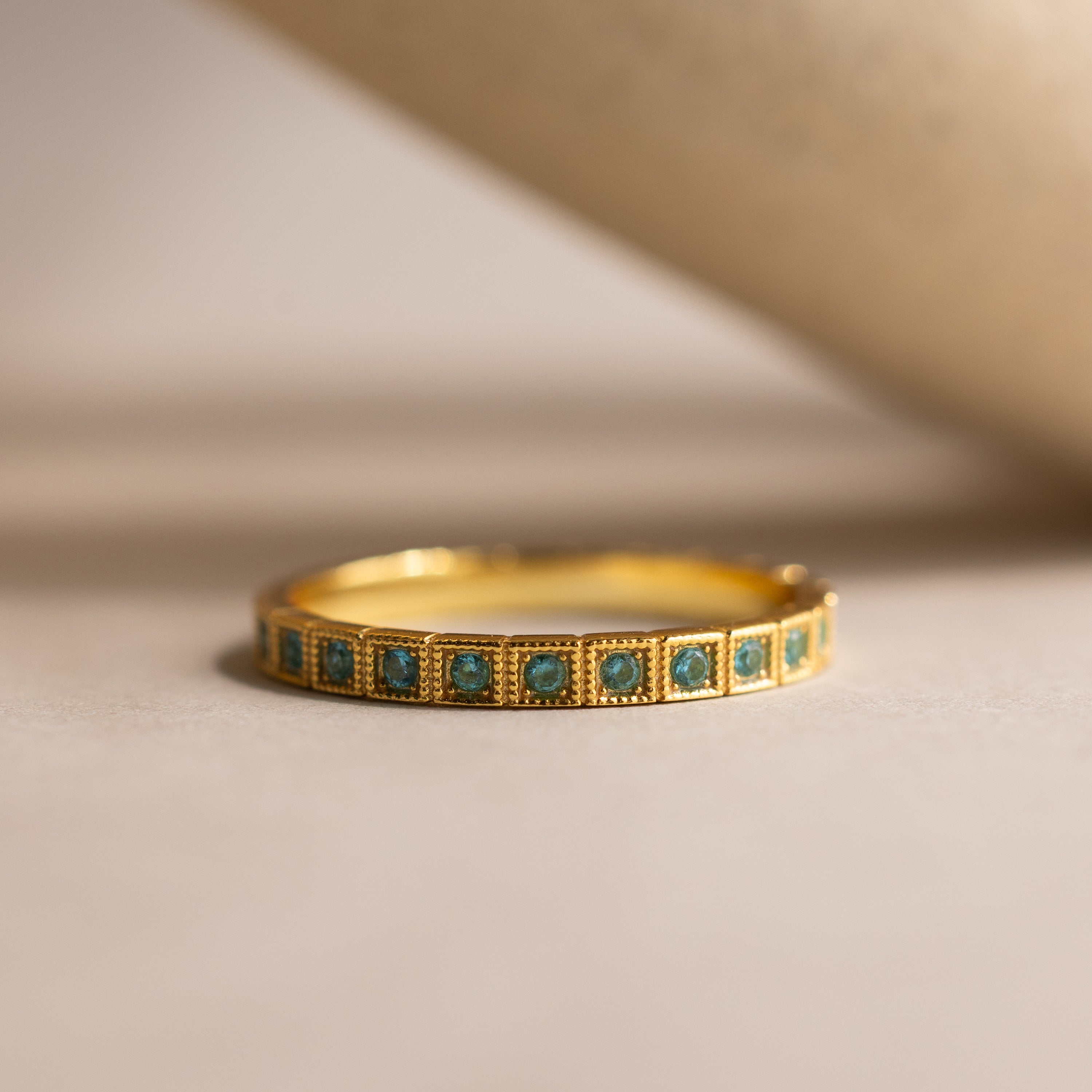 Art Deco Aquamarine Eternity Ring featuring a row of small square aquamarine stones set around the band, placed on a neutral surface.