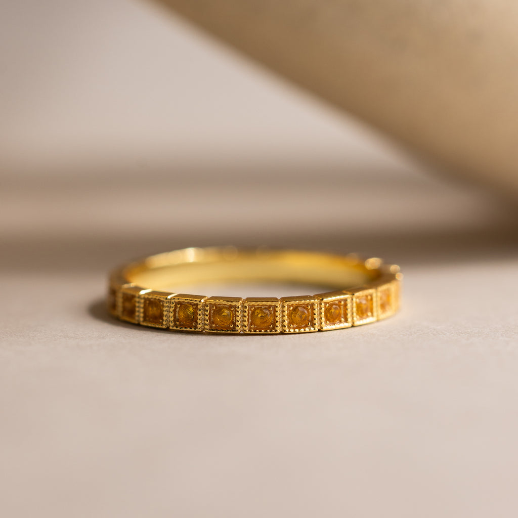 The Art Deco Topaz Eternity Ring, featuring a square-patterned design, rests on a smooth beige surface and exudes vintage-inspired elegance.