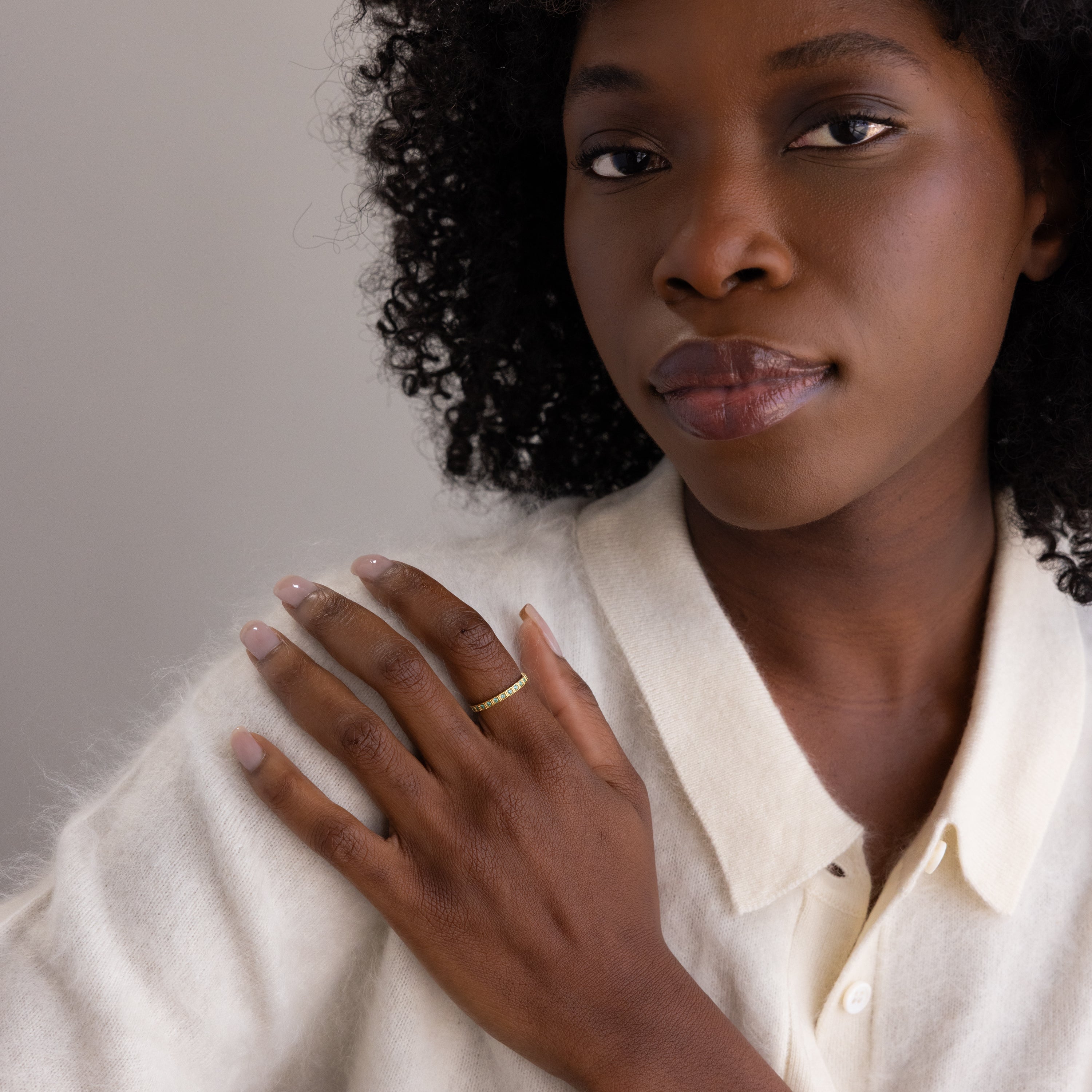 A woman with curly hair in a white shirt touches her shoulder, highlighting the Art Deco Aquamarine Eternity Ring on her finger.