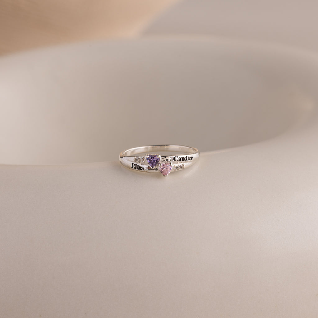 The Toi et Moi Interlocking Name Ring features two heart-shaped gemstones and engraved names, Elisa and Candice—a custom piece perfect for celebrating your unique bond.