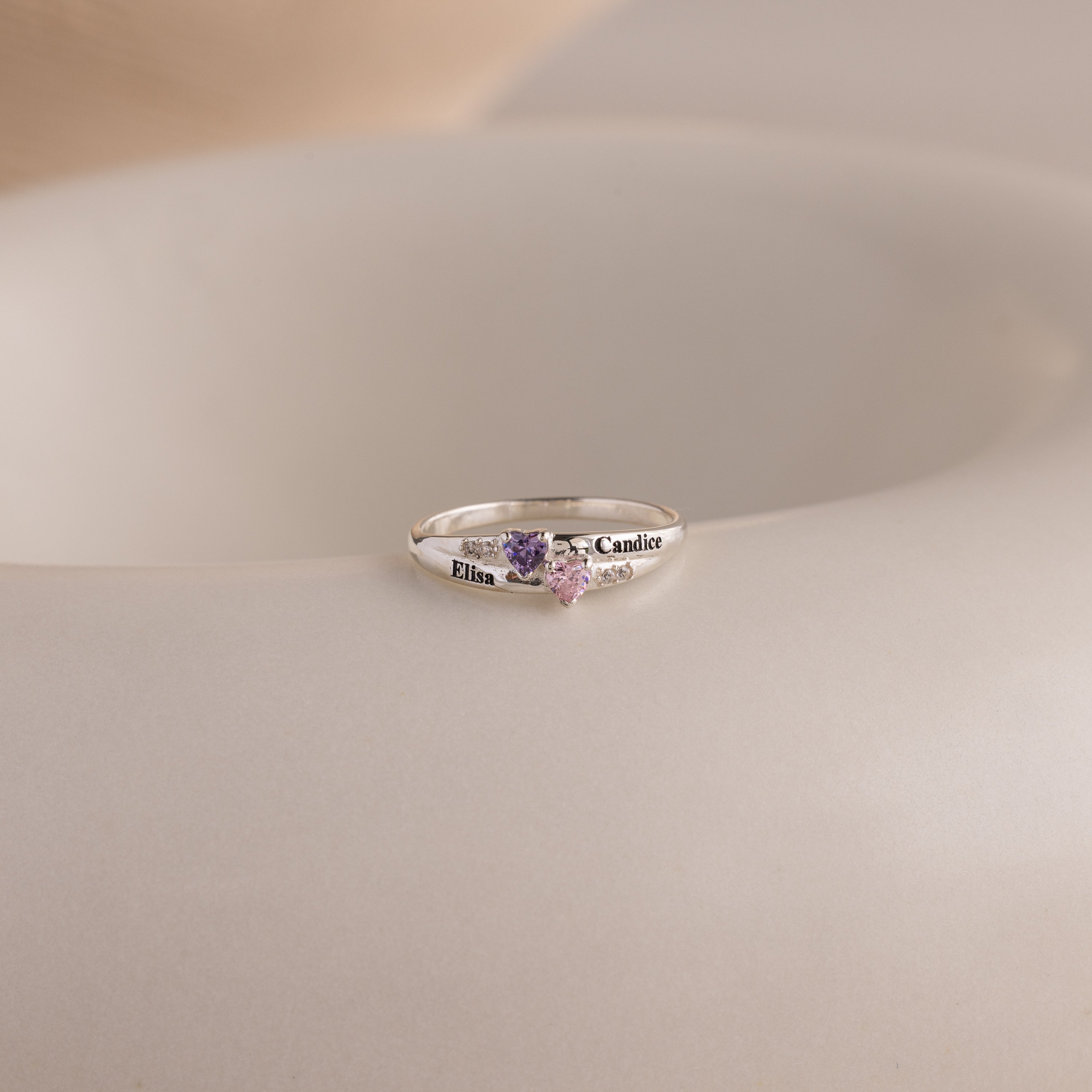 The Toi et Moi Interlocking Name Ring features two heart-shaped gemstones and engraved names, Elisa and Candice—a custom piece perfect for celebrating your unique bond.