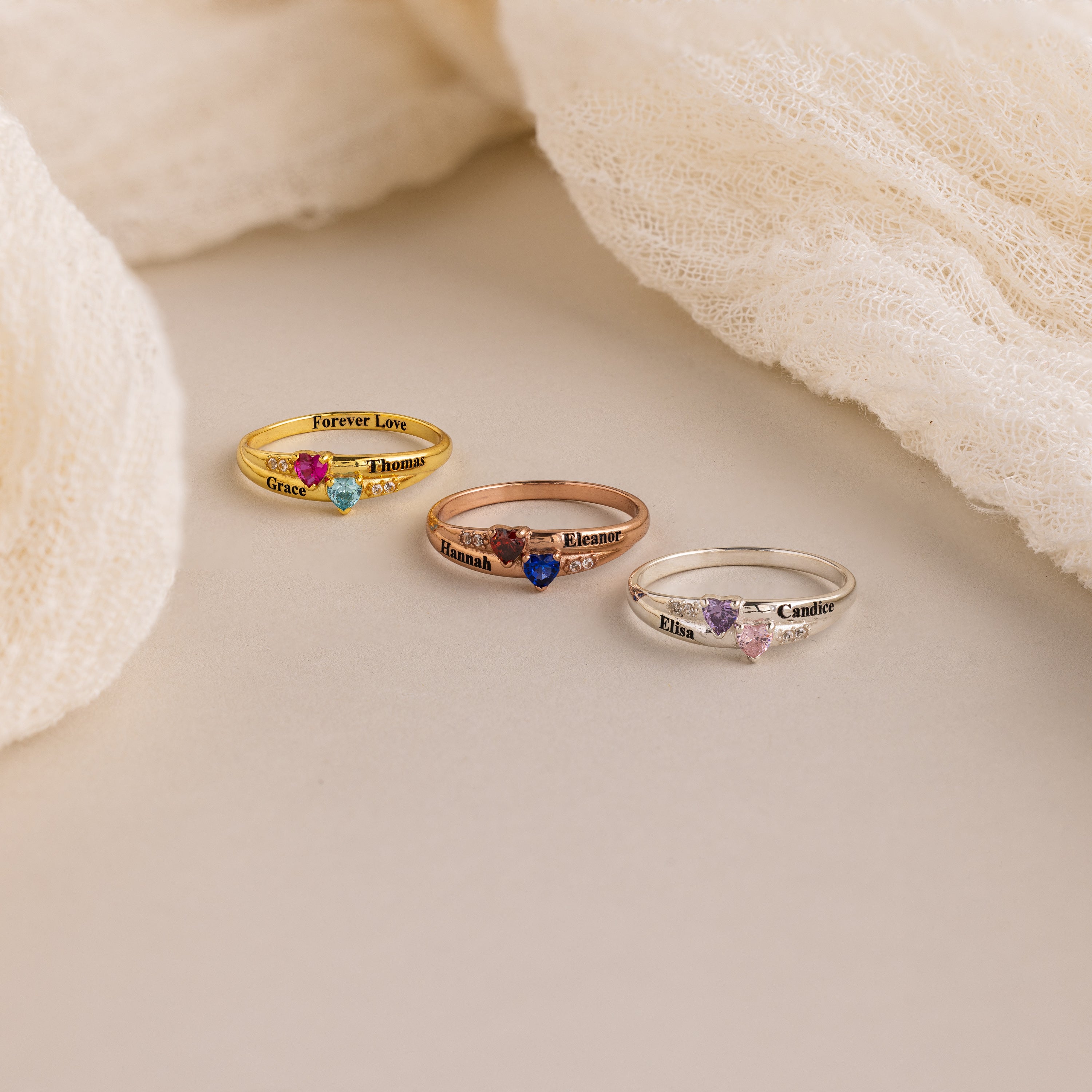 The Toi et Moi Interlocking Name Ring in Rose Gold, personalized with engraved names, is shown displayed on a soft beige fabric background.