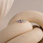 The Toi et Moi Interlocking Name Ring, featuring two heart-shaped birthstones and engraved names, rests on a beige, twisted sculpture.