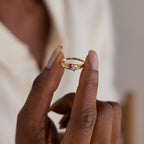 A hand holding the Toi et Moi Interlocking Name Ring, featuring gold, three colorful gemstones, and engraved text—perfect as a custom name ring.