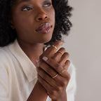 A woman with curly hair gazes upward, wearing a cream-colored top and displaying the 18K gold Toi et Moi Interlocking Name Ring on her fingers.