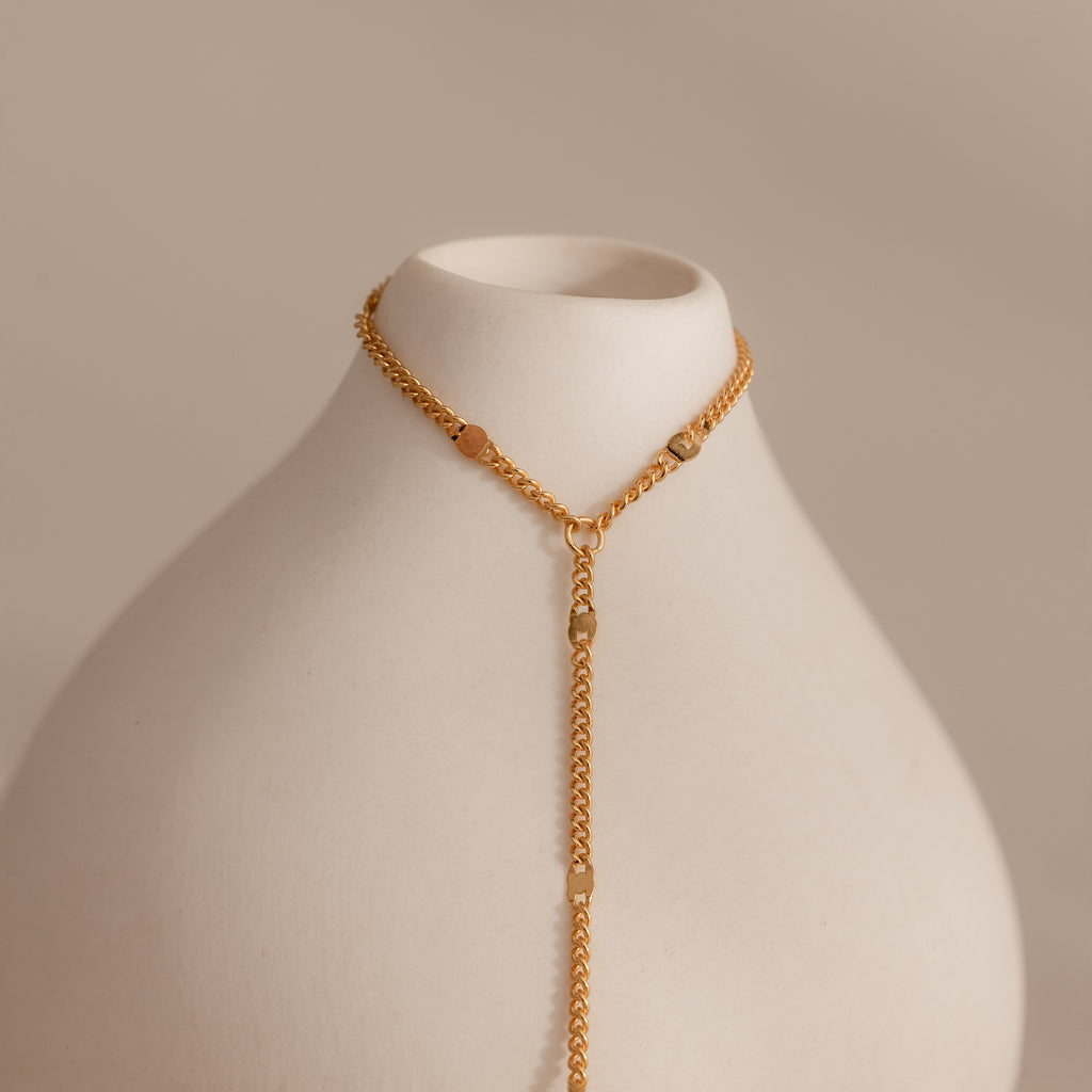 Curb hand chain bracelet in 18K gold displayed on a white ceramic prop.