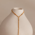 Curb hand chain bracelet in 18K gold displayed on a white ceramic prop.