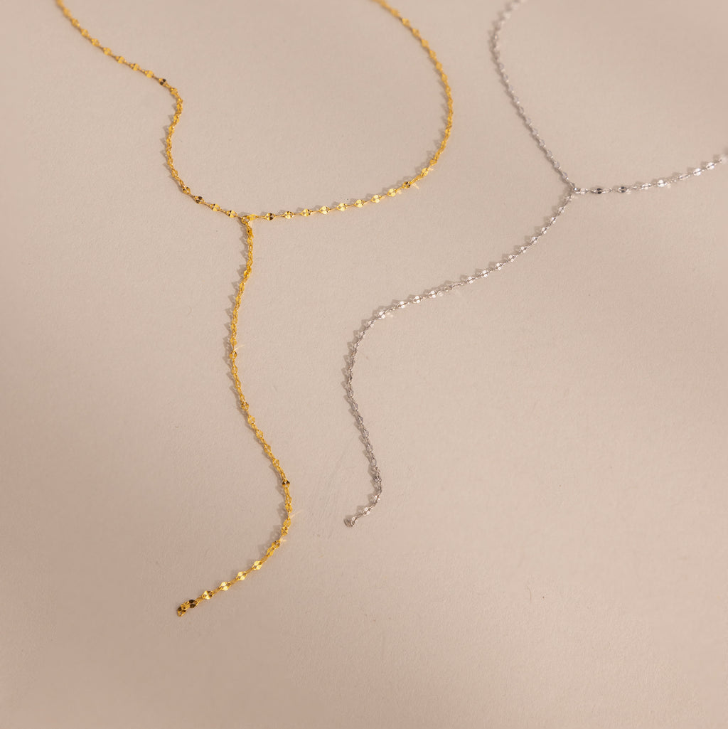 Flat-lay of two mirror chain lariat necklaces in gold and silver, showcasing the dainty and reflective design.