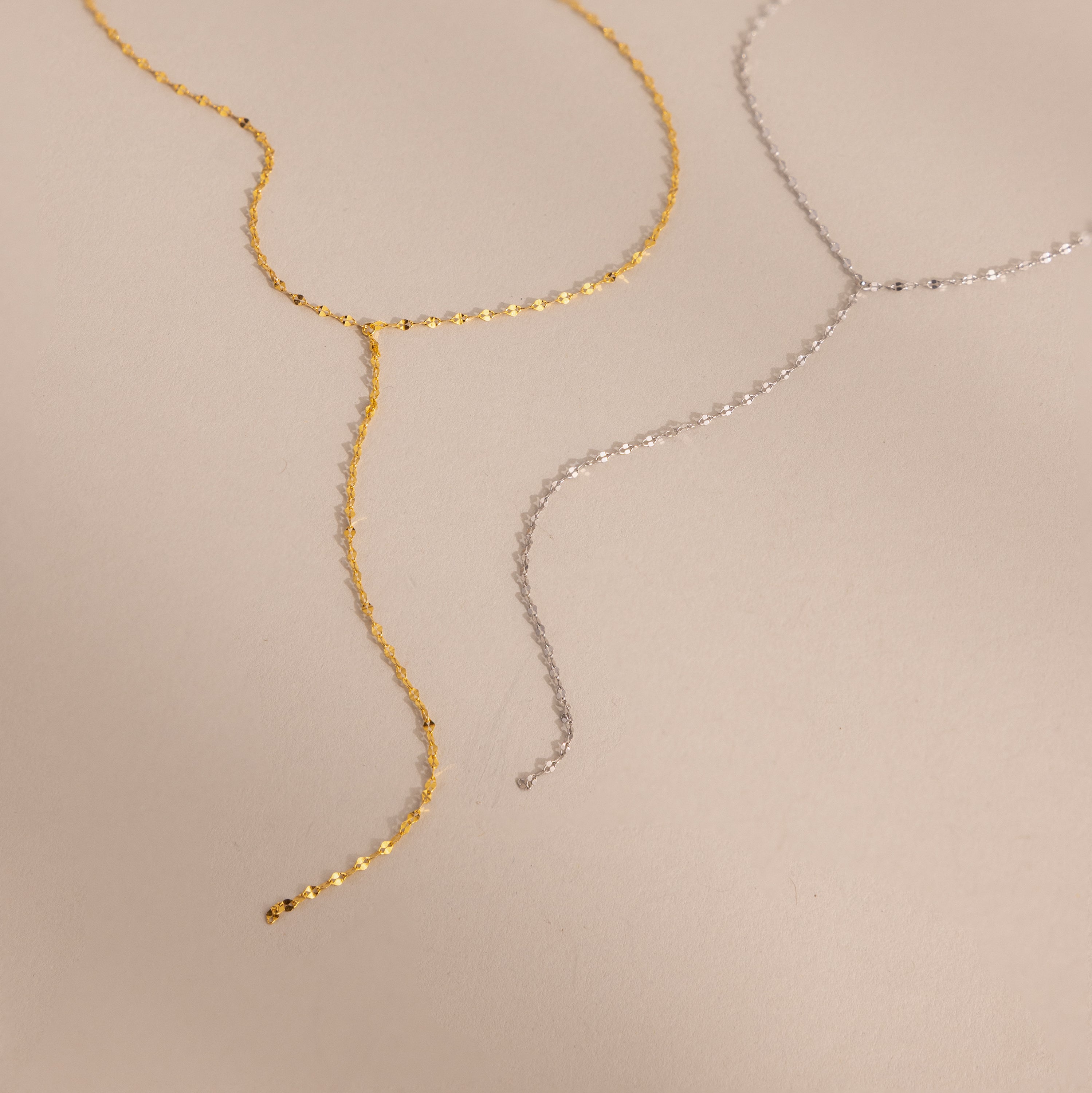 Flat-lay of two mirror chain lariat necklaces in gold and silver, showcasing the dainty and reflective design.