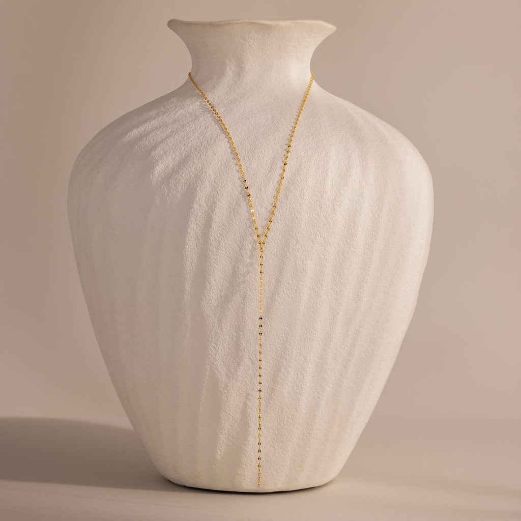 Gold dainty mirror chain lariat necklace displayed on a white ceramic vase.